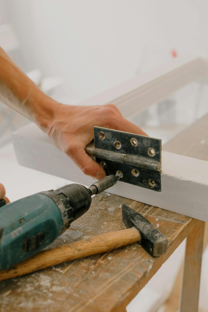 A person attaching a door hinge with a drill.